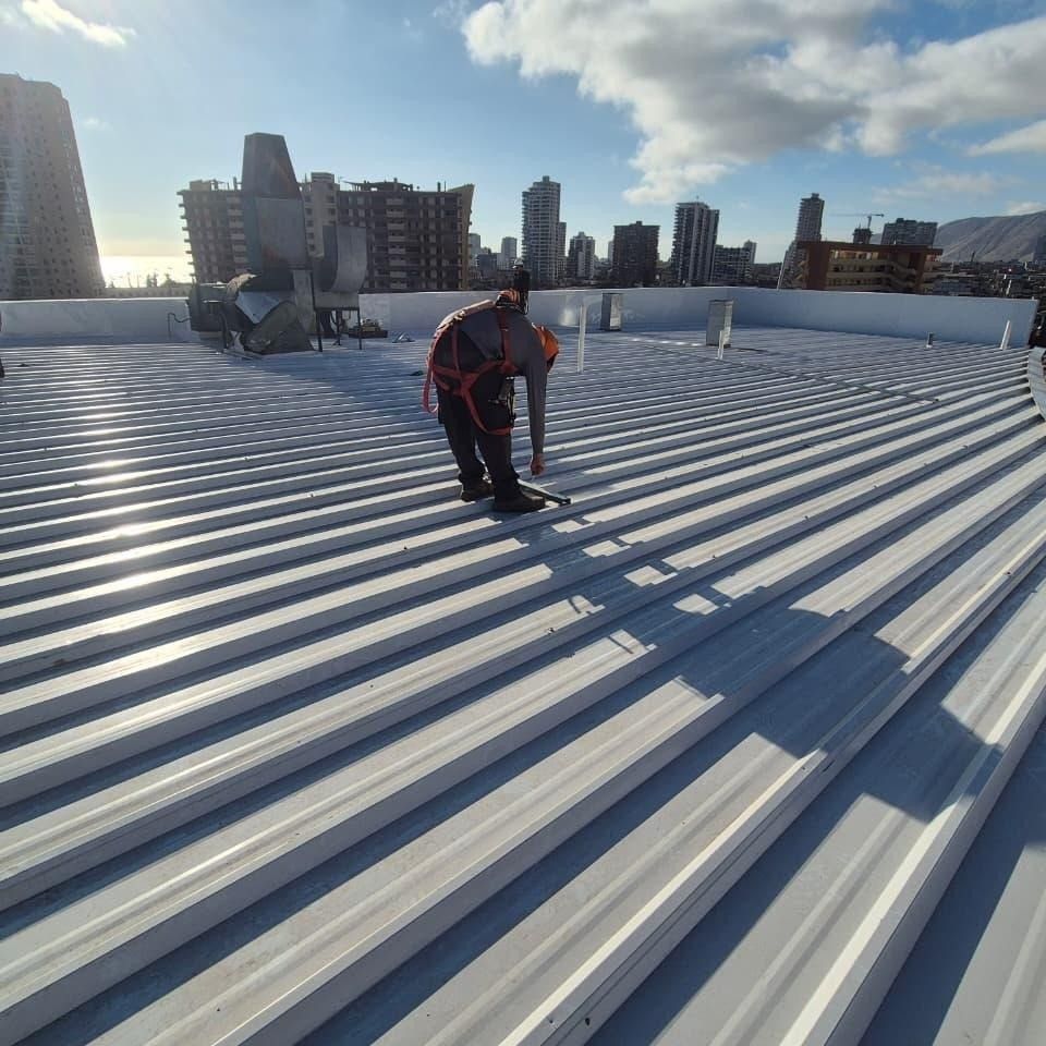 Técnico con arnés instalando cubierta metálica nueva sobre un edificio en Iquique