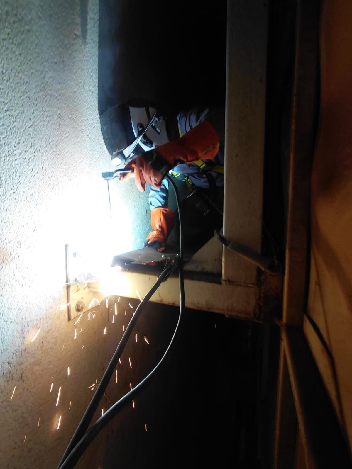 Soldador con equipo de protección trabajando en una estructura metálica en altura