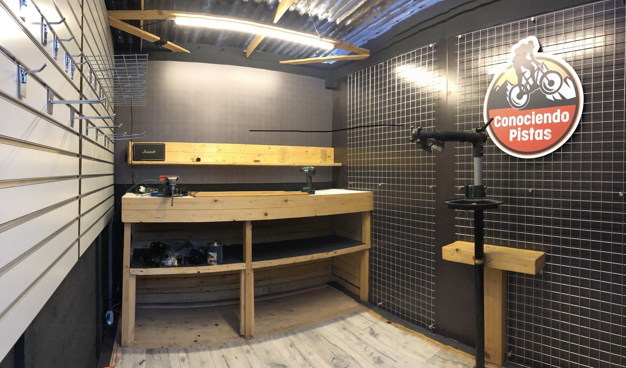 Taller de bicicletas con mobiliario a medida: mesón de trabajo en madera, panel ranurado y rejilla de exhibición